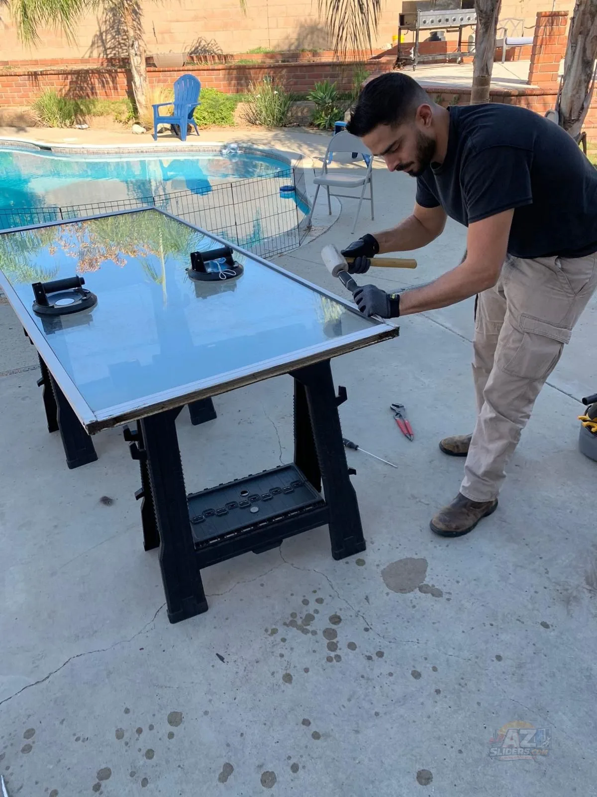 Technician servicing sliding glass door panel on sawhorses by pool — Mesa AZ repair by AZSliders